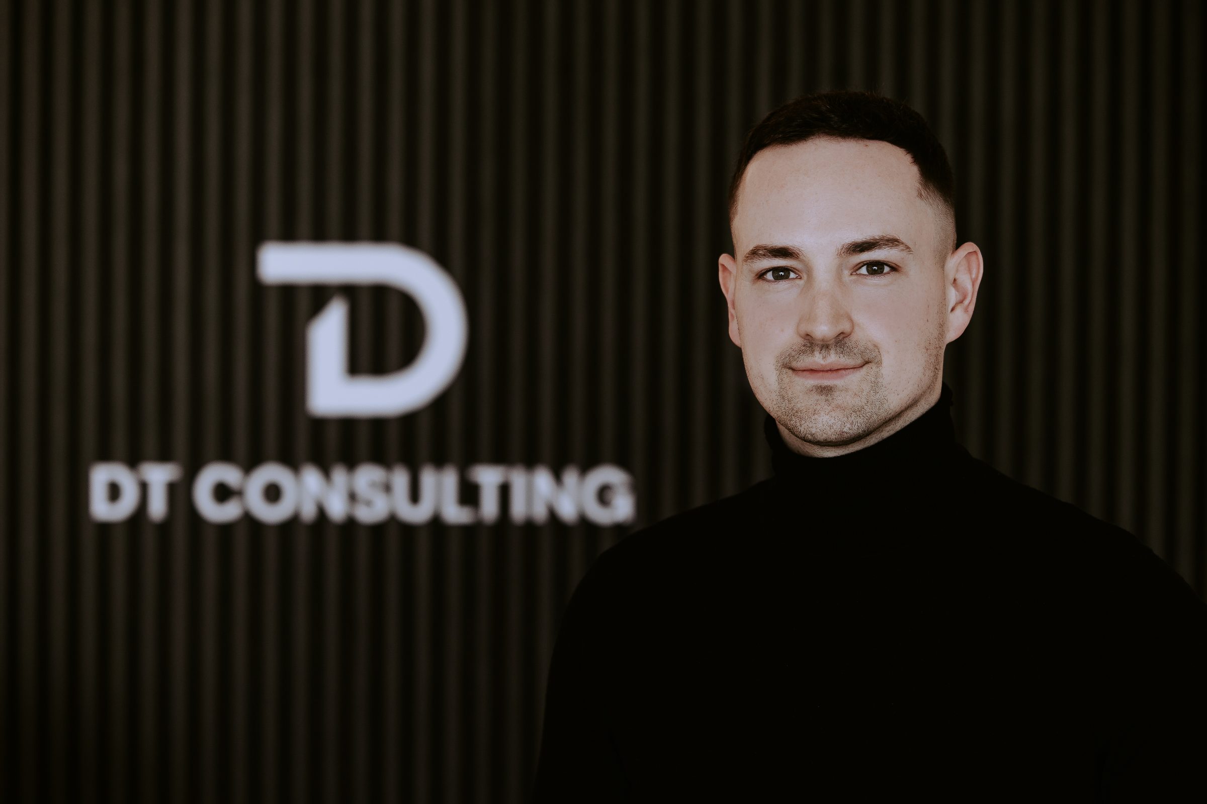 Danny Tillmann im Büro von DT Consulting vor der beleuchteten Logo-Wand